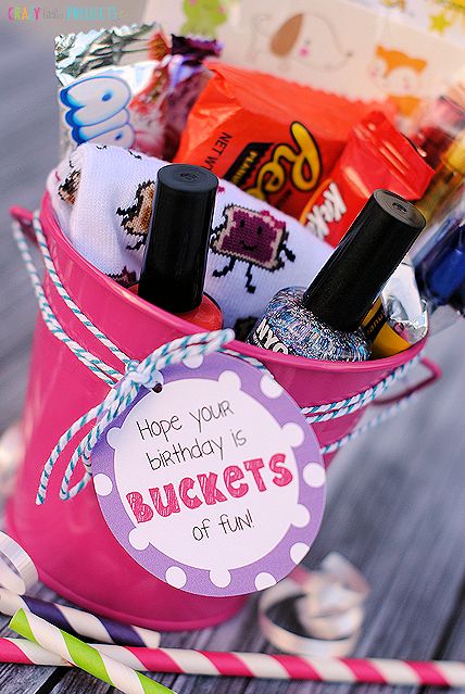 a pink bucket filled with lots of candy and personalized birthday items on a wooden table