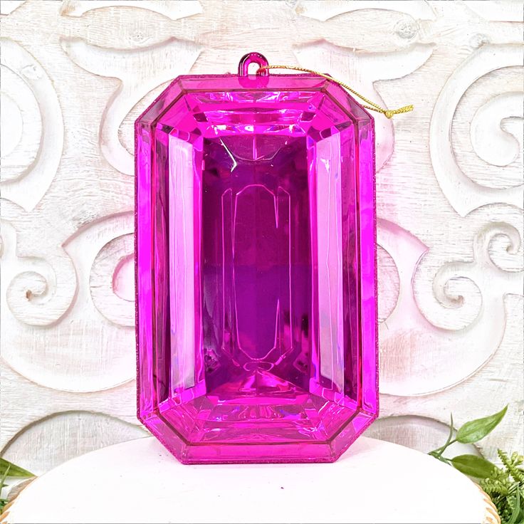 a large pink jewel sitting on top of a white table next to green planters