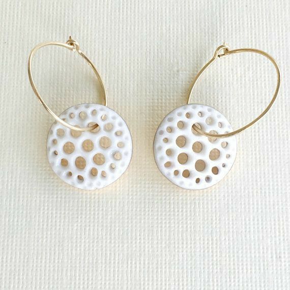 two white and gold earrings with dots on them sitting on top of a white surface