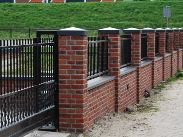 a brick wall with black iron fence and green grass in the backgrouds