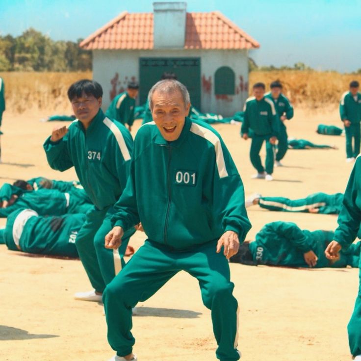 a group of men standing around each other on top of a dirt field in front of a building