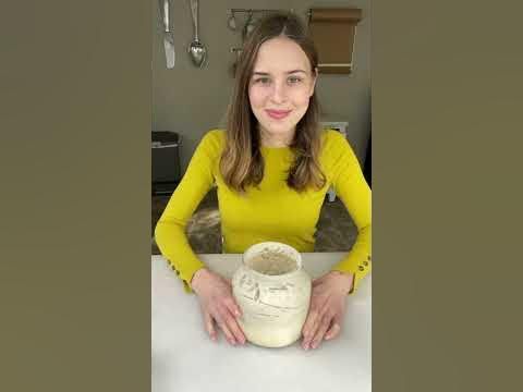 a woman in yellow shirt holding a vase on top of a white table with utensils