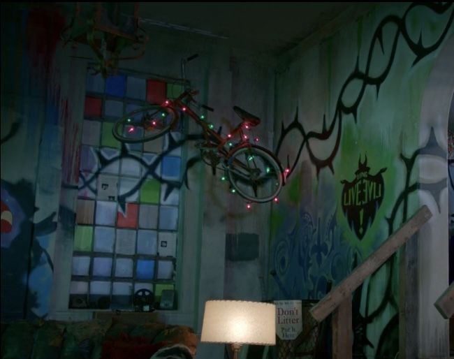 a living room with graffiti on the walls and a bicycle hanging from the ceiling, next to a lamp