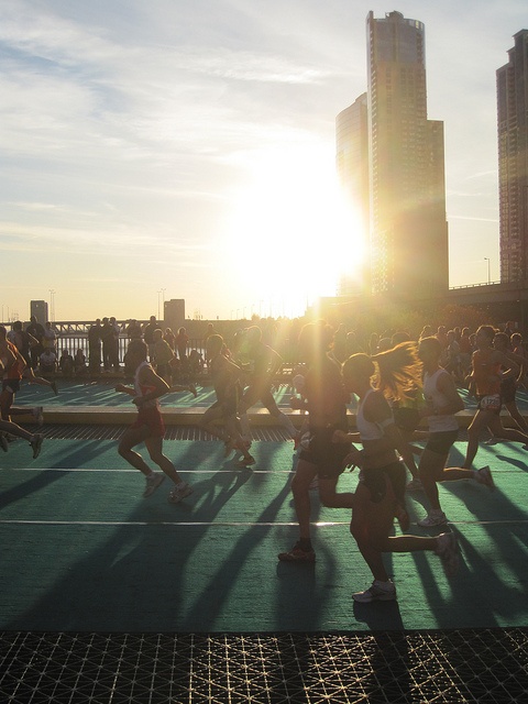 a group of people running on top of a tennis court in front of tall buildings