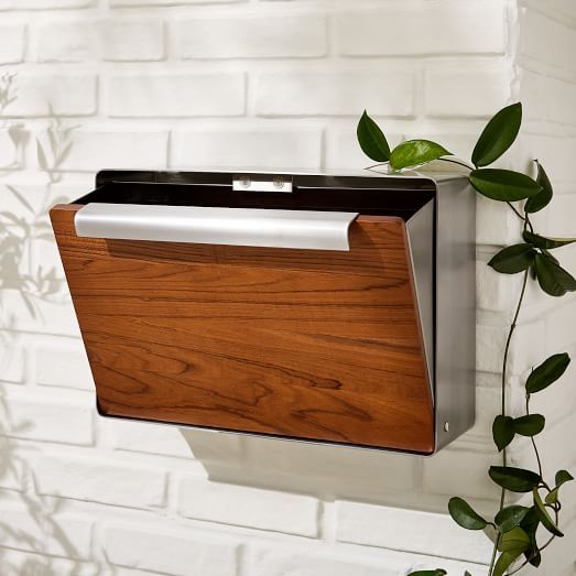 a metal and wood folder holder hanging on a white brick wall next to a green plant