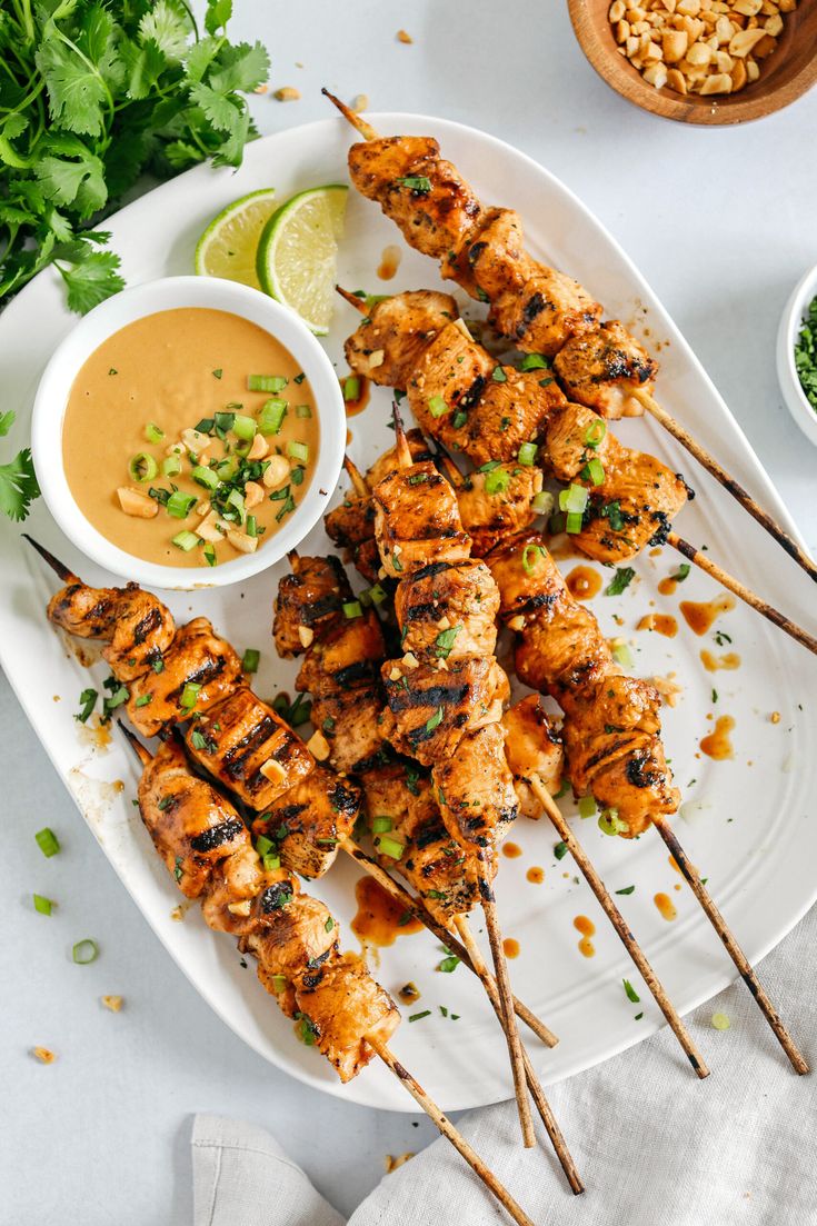 grilled chicken skewers on a plate with dipping sauce and cilantro