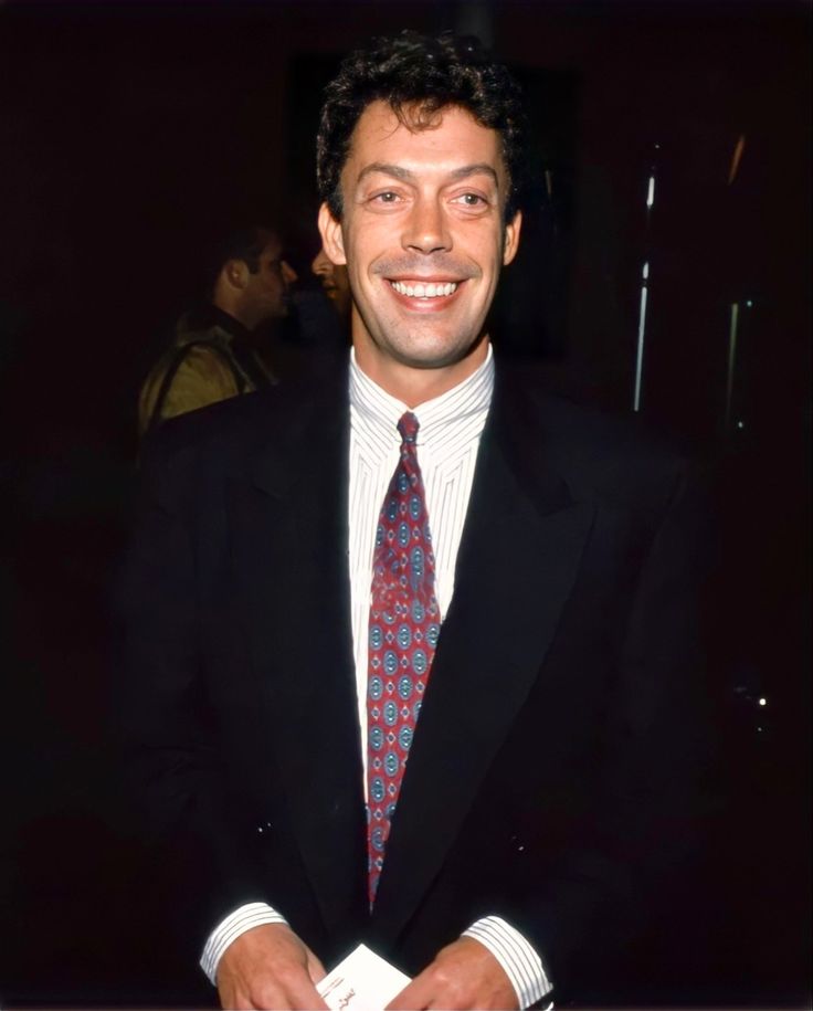 a man in a suit and tie smiling at the camera with his hands folded over his chest