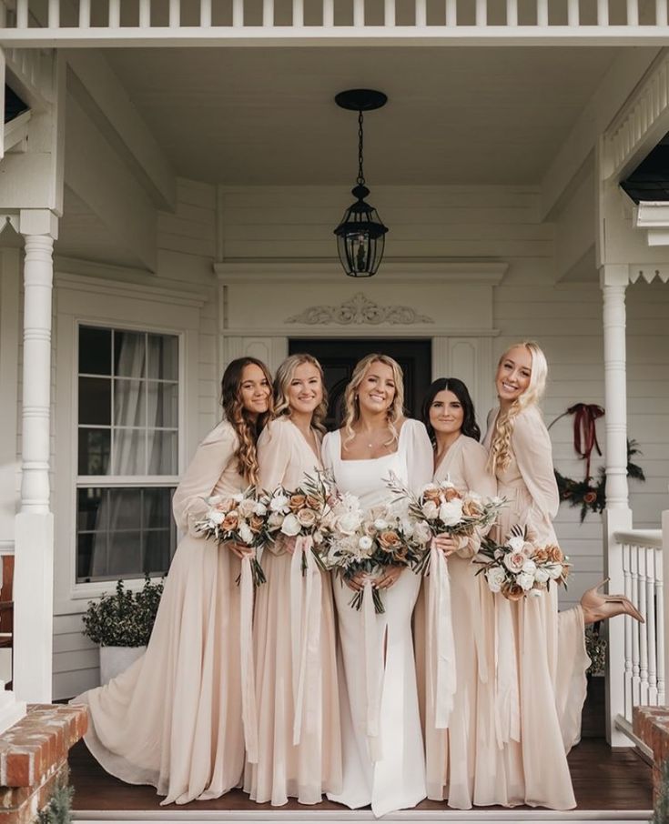 a group of women standing next to each other in front of a white house holding bouquets