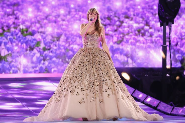 a woman in a gown on stage singing into a microphone with purple lights behind her