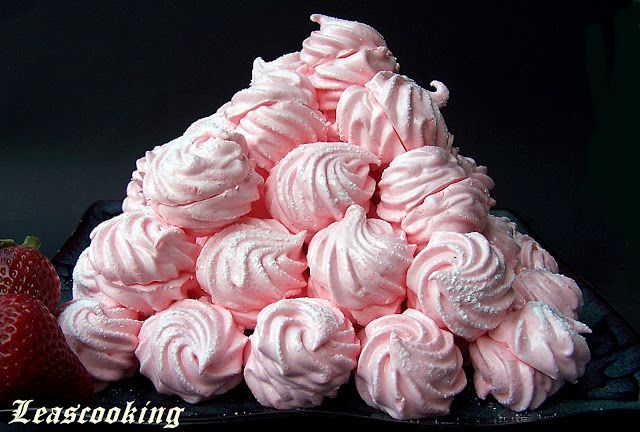 a pile of pink frosted mering next to a strawberry on a black plate