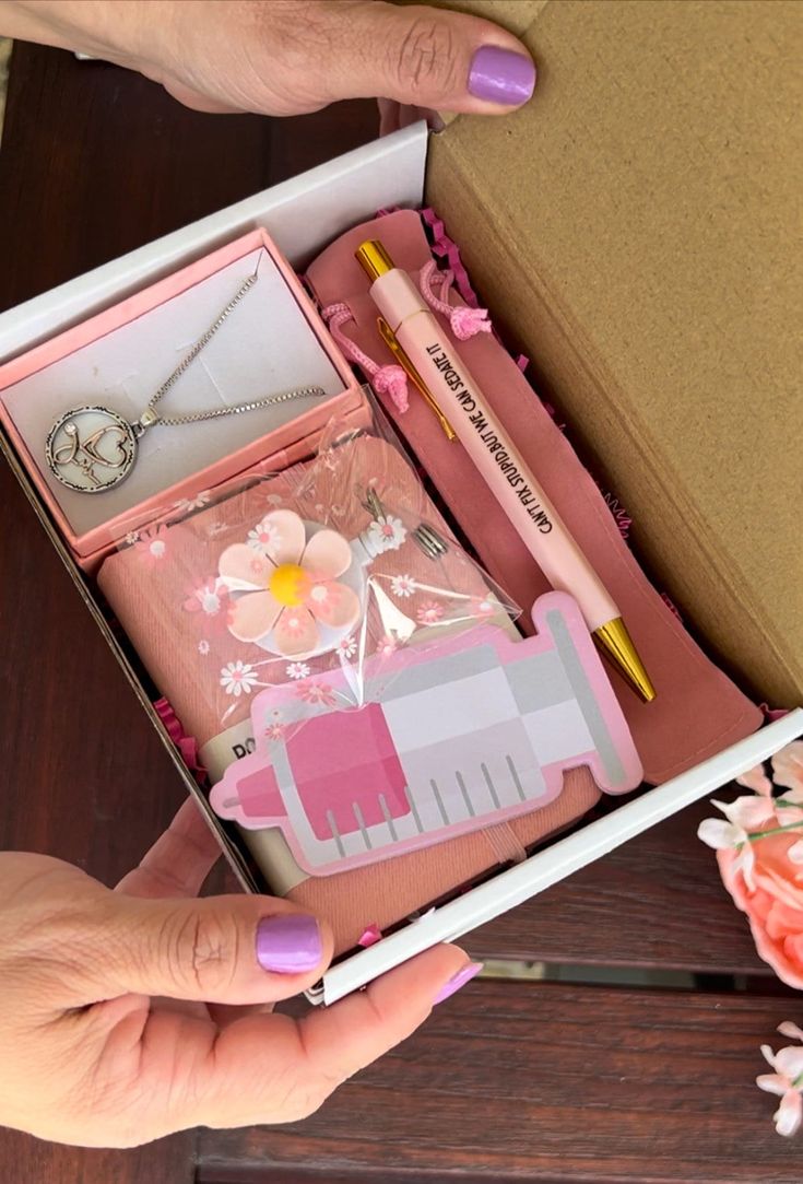 a woman's hands holding an open pink box with various items inside