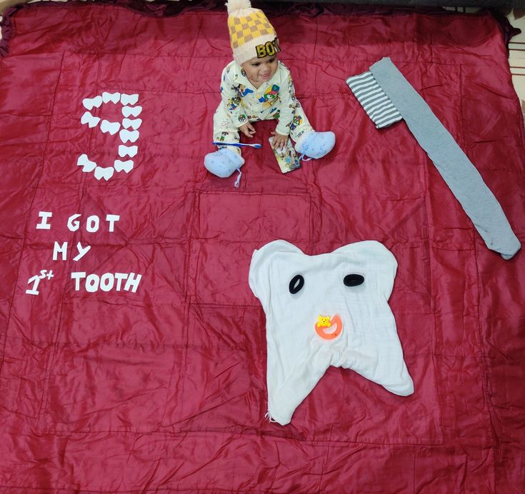 a baby laying on top of a red blanket next to toothbrushes and other items