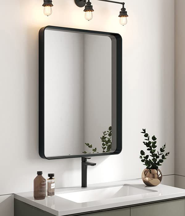 a bathroom vanity with a mirror and lights on it's side, next to a plant