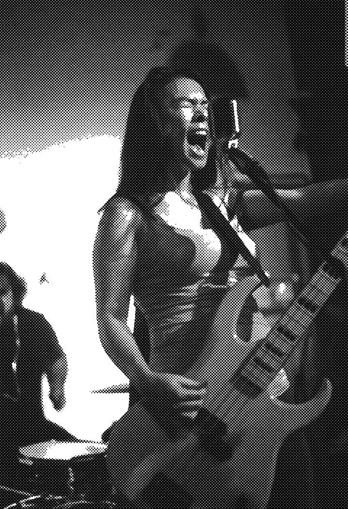 a woman playing guitar and singing into a microphone while another man plays drums behind her