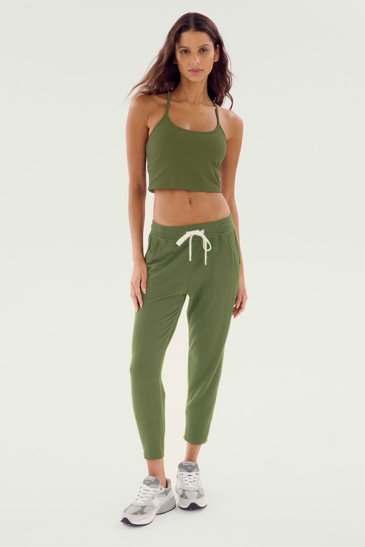 A woman stands against a plain background wearing a green crop top made with soft modal fabric, the SPLITS59 Reena Fleece 7/8 Sweatpant in Olive/White, and white sneakers. Green Joggers For Fall Loungewear, Sporty Green Joggers For Fall, Green Athleisure Sweats For Jogging, Green Athleisure Joggers With Ribbed Cuffs, Green Relaxed Fit Sporty Activewear, Solid Color Sportswear Sweats For Loungewear, Sporty Green Relaxed Fit Activewear, Sporty Green Joggers With Ribbed Cuffs, Green Cotton Activewear For Jogging