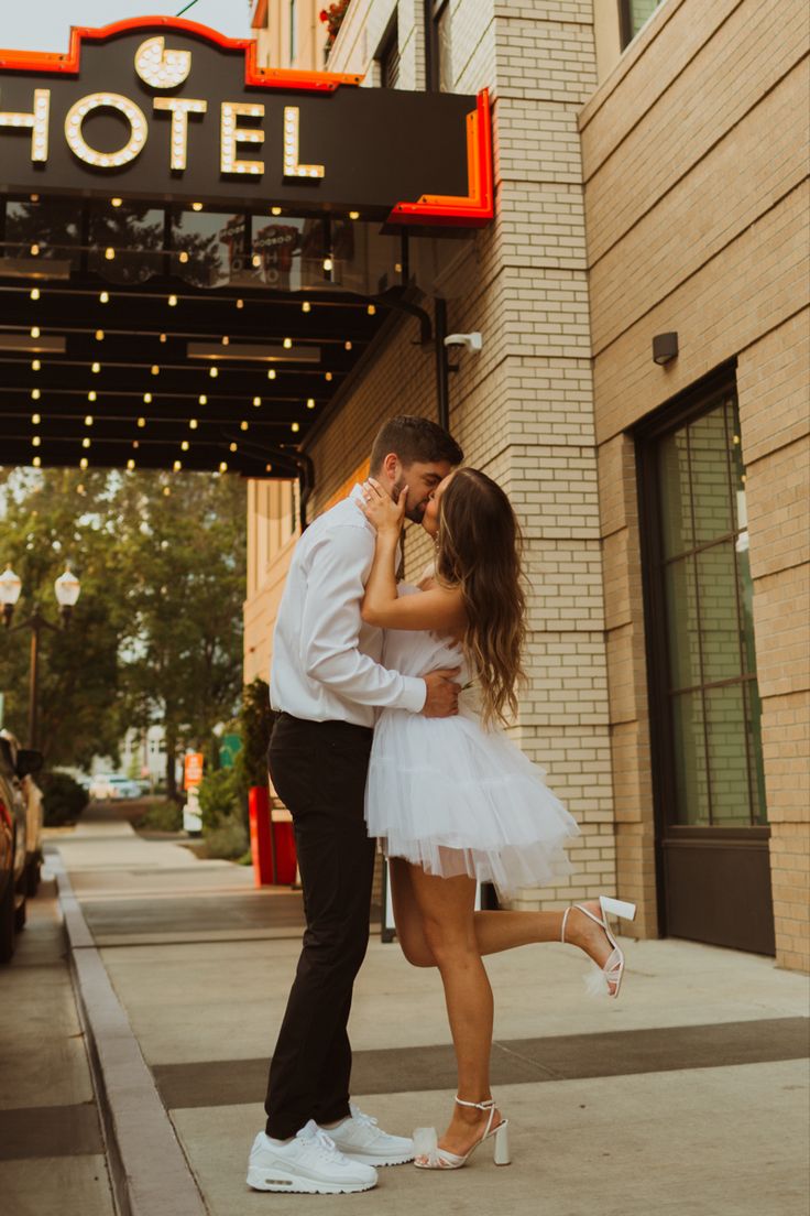 a man and woman kissing in front of a hotel