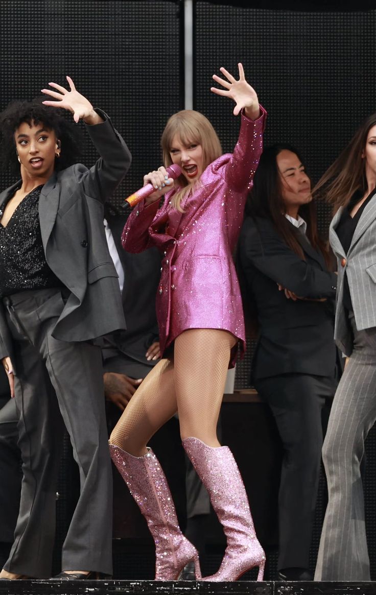 taylor swift performing on stage with her hands in the air and other people behind her