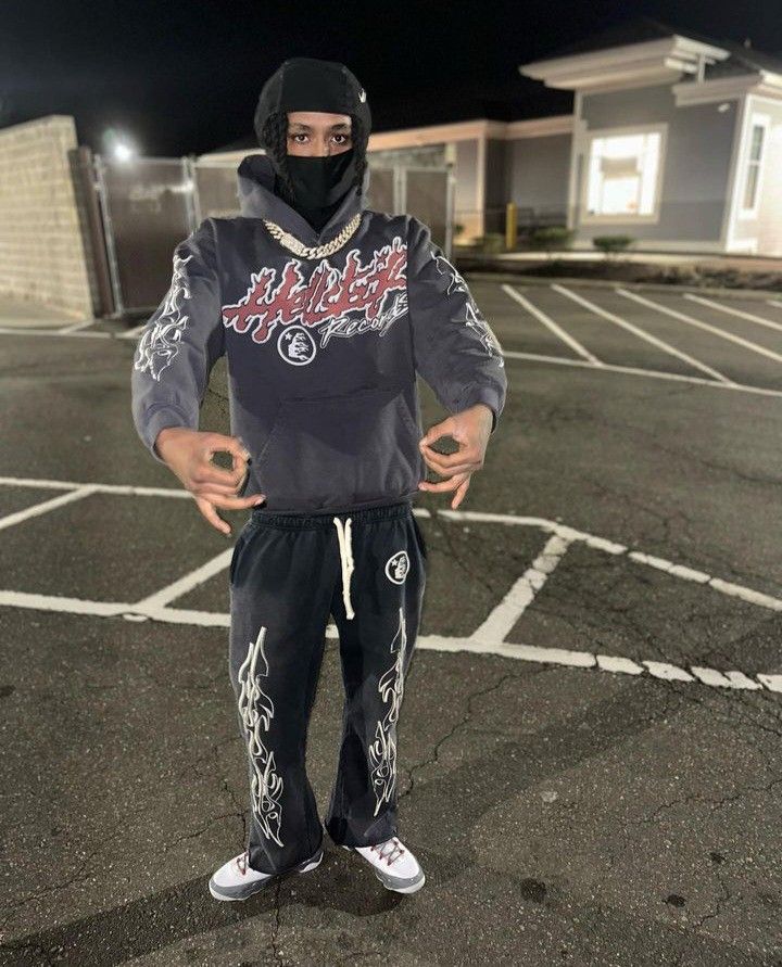 a man wearing a hoodie and sweatpants stands in a parking lot at night