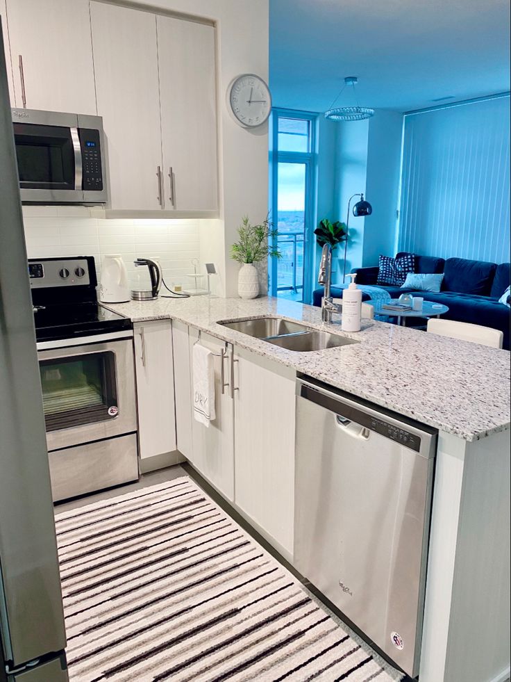 a clean kitchen with stainless steel appliances and white cabinets, striped rug on the floor