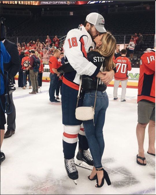 a man and woman kissing on the ice at an indoor hockey rink with fans in the stands