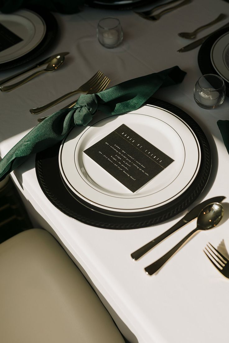 a place setting with silverware and green napkins on a white tableclothed table