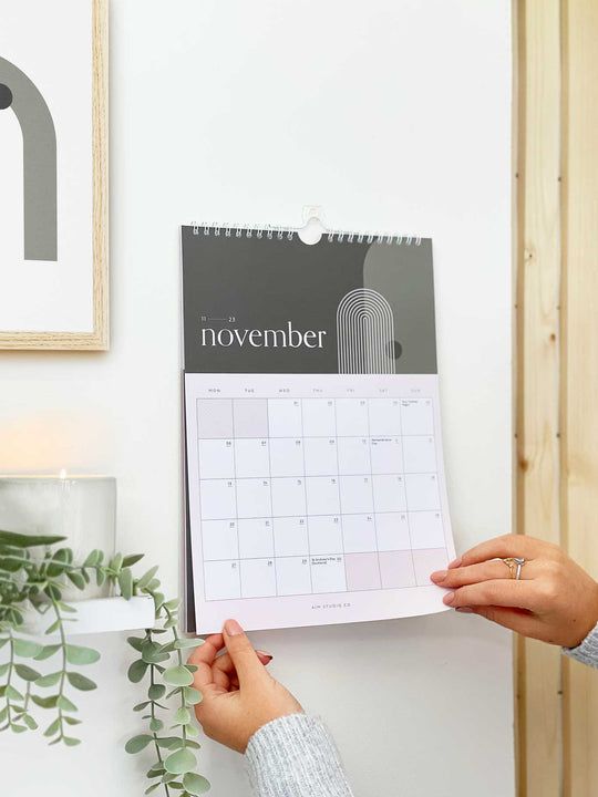 a person holding a calendar in front of a wall with plants and candles on it