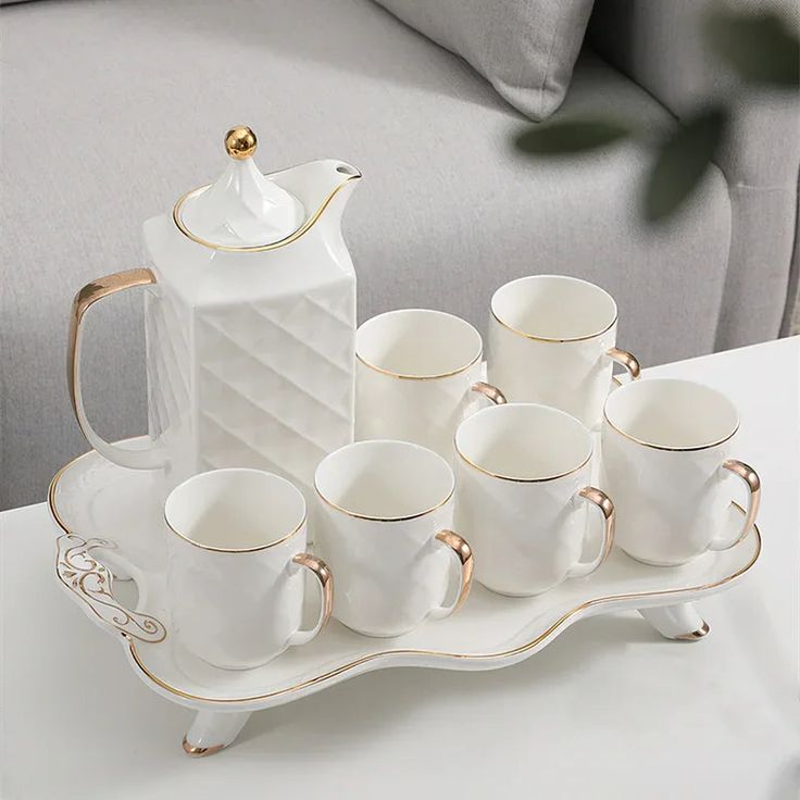 a tray with coffee cups and a tea pot on it, sitting on a couch