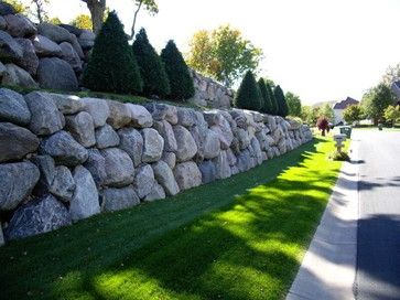 a large rock wall along the side of a road with grass growing on both sides