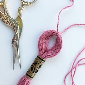 two pairs of scissors and pink thread on a white surface with gold trimmings