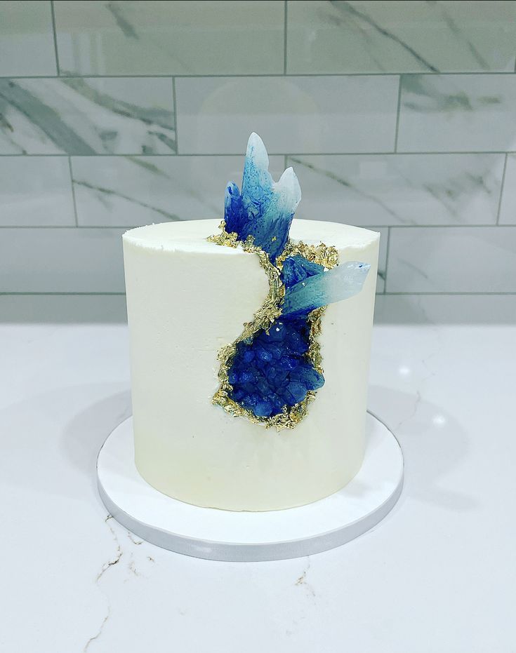 a white cake with blue frosting and gold sprinkles sitting on top of a counter