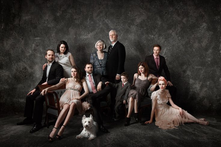 a group of people sitting next to each other in front of a gray wall with a dog