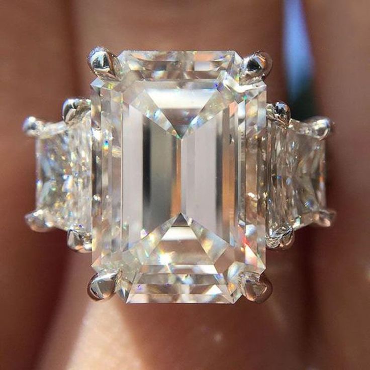 a woman's hand holding an emerald and three stone ring with diamonds on it