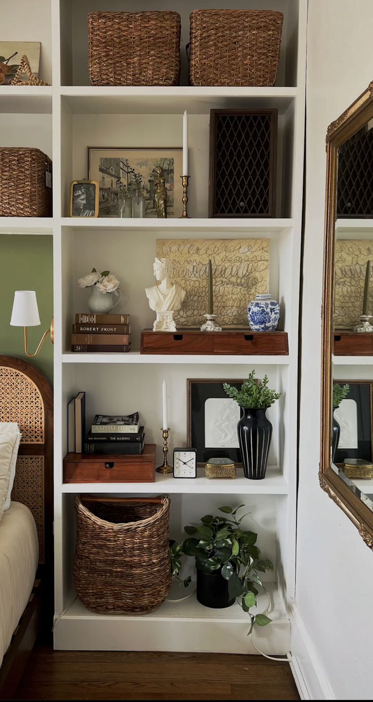 a white book shelf filled with lots of books next to a mirror and lamp on top of a wooden floor