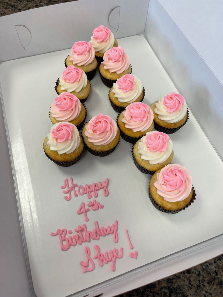 cupcakes with pink frosting are arranged in a square box on a table