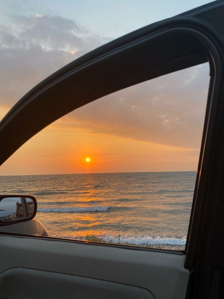 the sun is setting over the ocean as seen from inside a car