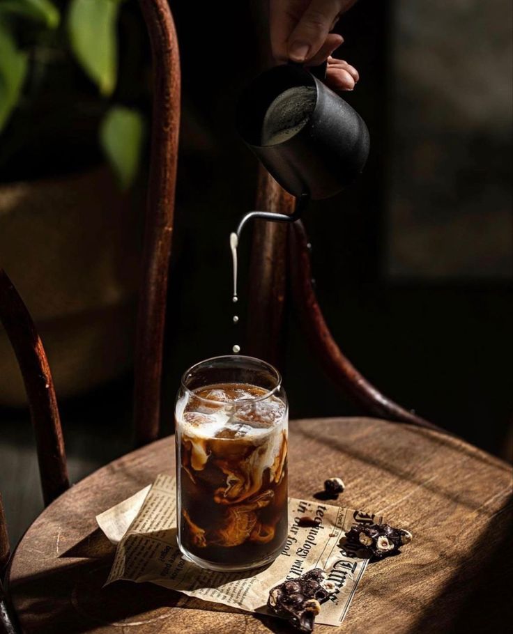 a person pouring coffee into a glass on top of a wooden table