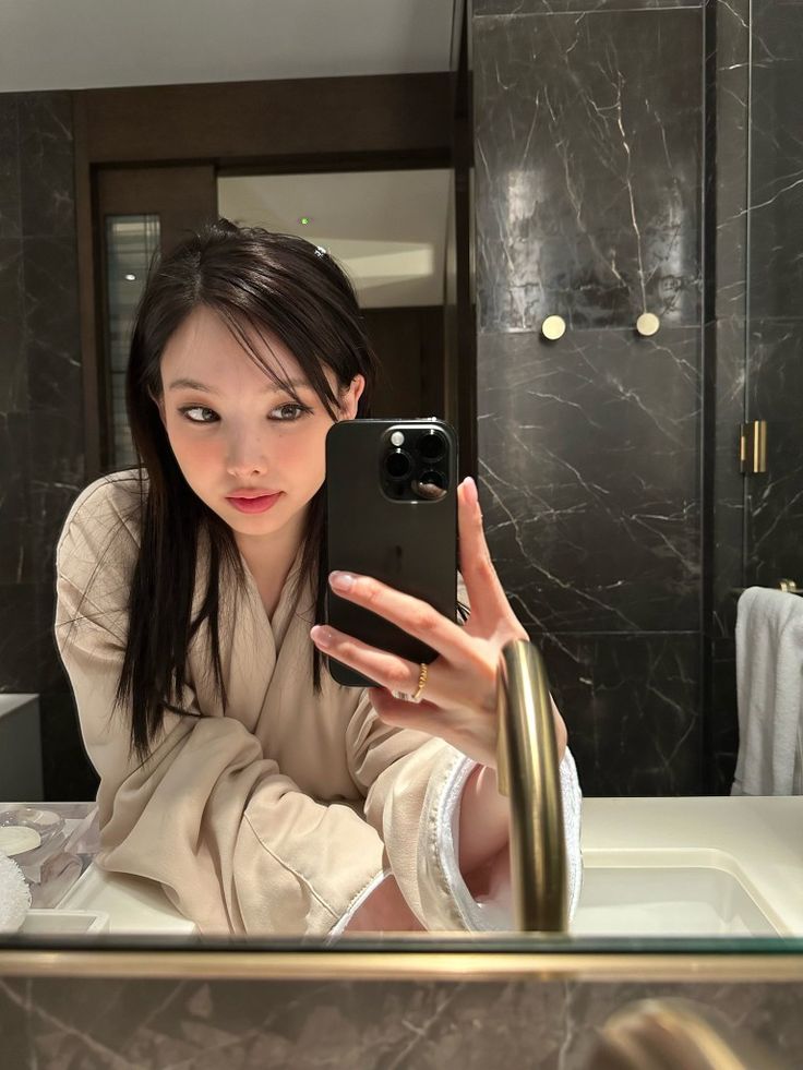 a woman taking a selfie in front of a bathroom mirror with her cell phone