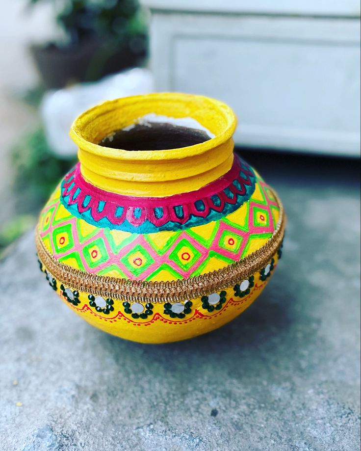 a brightly colored vase sitting on top of a cement floor next to a planter