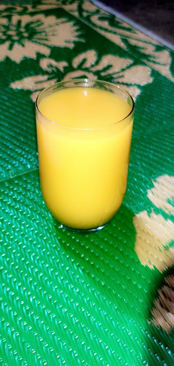 a glass filled with orange juice sitting on top of a green mat