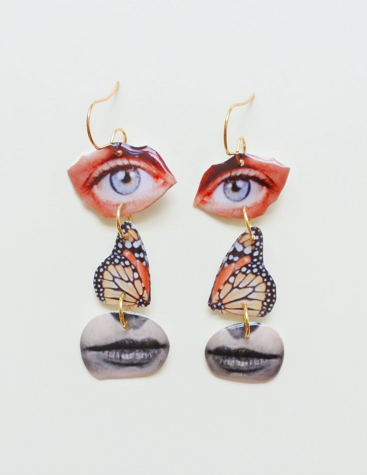 a pair of earrings with an eye and butterfly on it's ear ends, hanging from gold - plated hooks