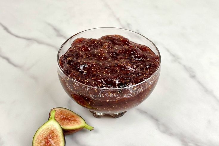 a glass bowl filled with jam next to sliced figs on a marble counter top