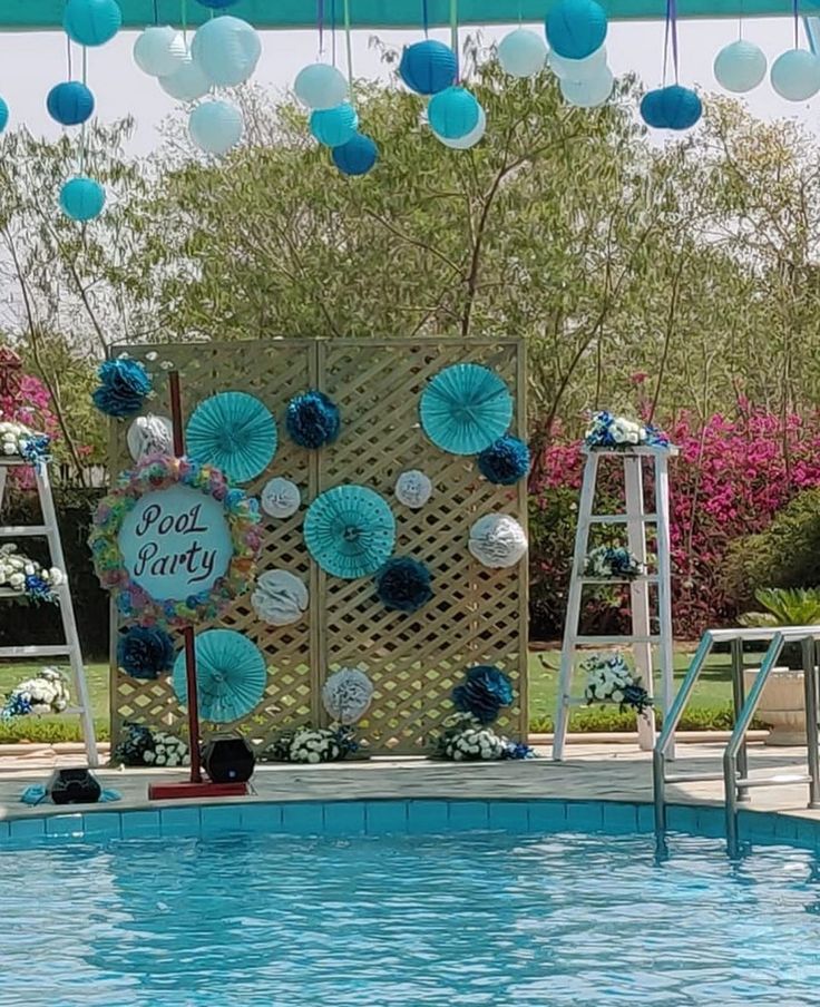 an outdoor pool decorated with blue and white paper fans, flowers and decorations for a pool party