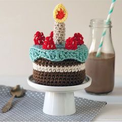 a crocheted birthday cake sitting on top of a table next to a bottle