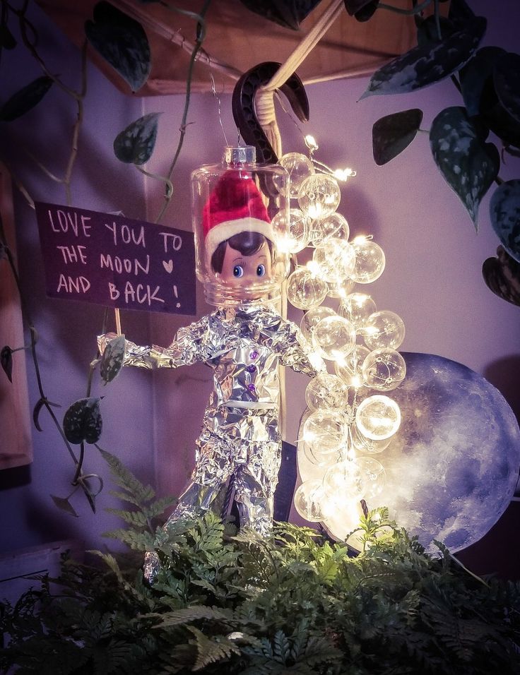 an elf is holding a sign in front of a tree with lights and bubbles on it