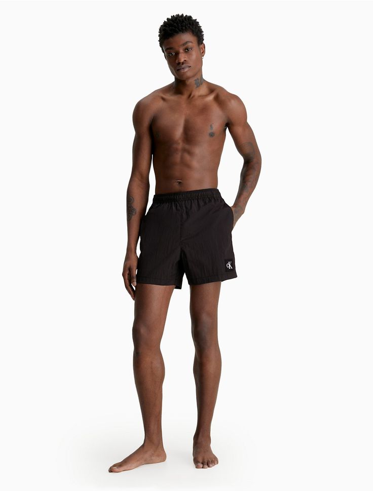 a man standing in front of a white background wearing black swim trunks and no shirt