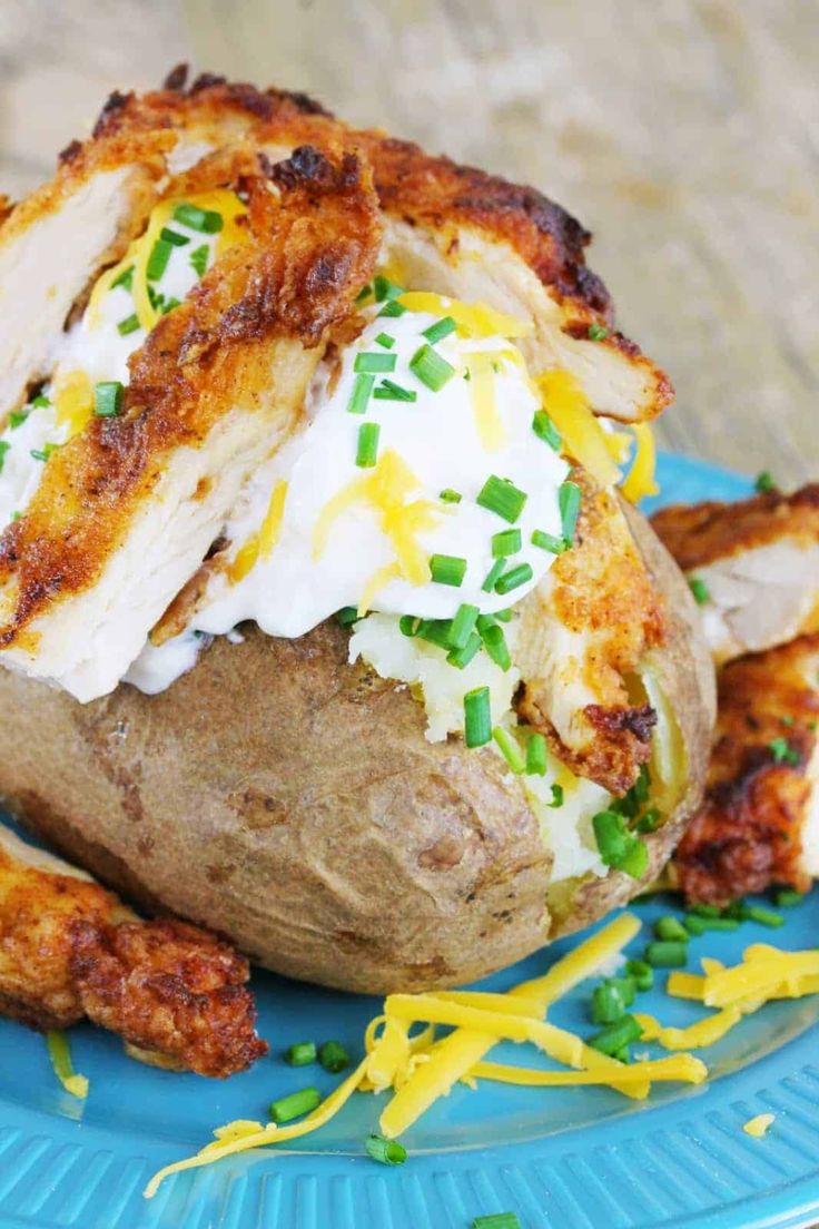 a baked potato with chicken and cheese on it sitting on a blue plate next to some green sprinkles