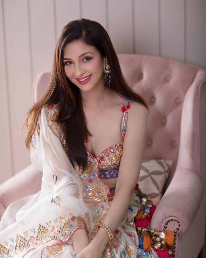 a woman sitting in a pink chair wearing a dress and smiling with her legs crossed