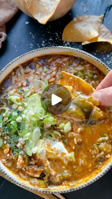 a hand dipping some food into a bowl with tortilla chips on the side