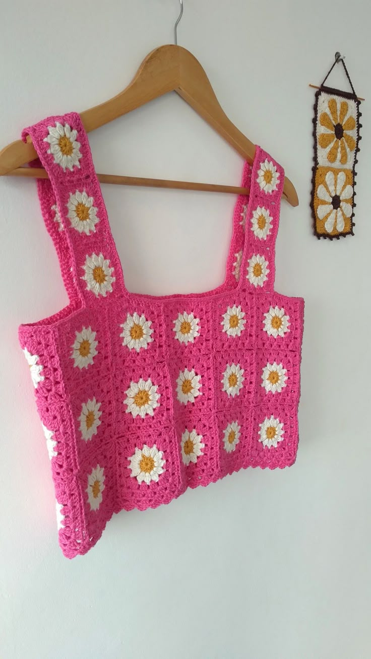 a pink crocheted top hanging on a wall next to a wooden hanger