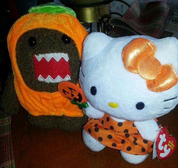 two hello kitty stuffed animals sitting next to each other on a wooden table with pumpkins